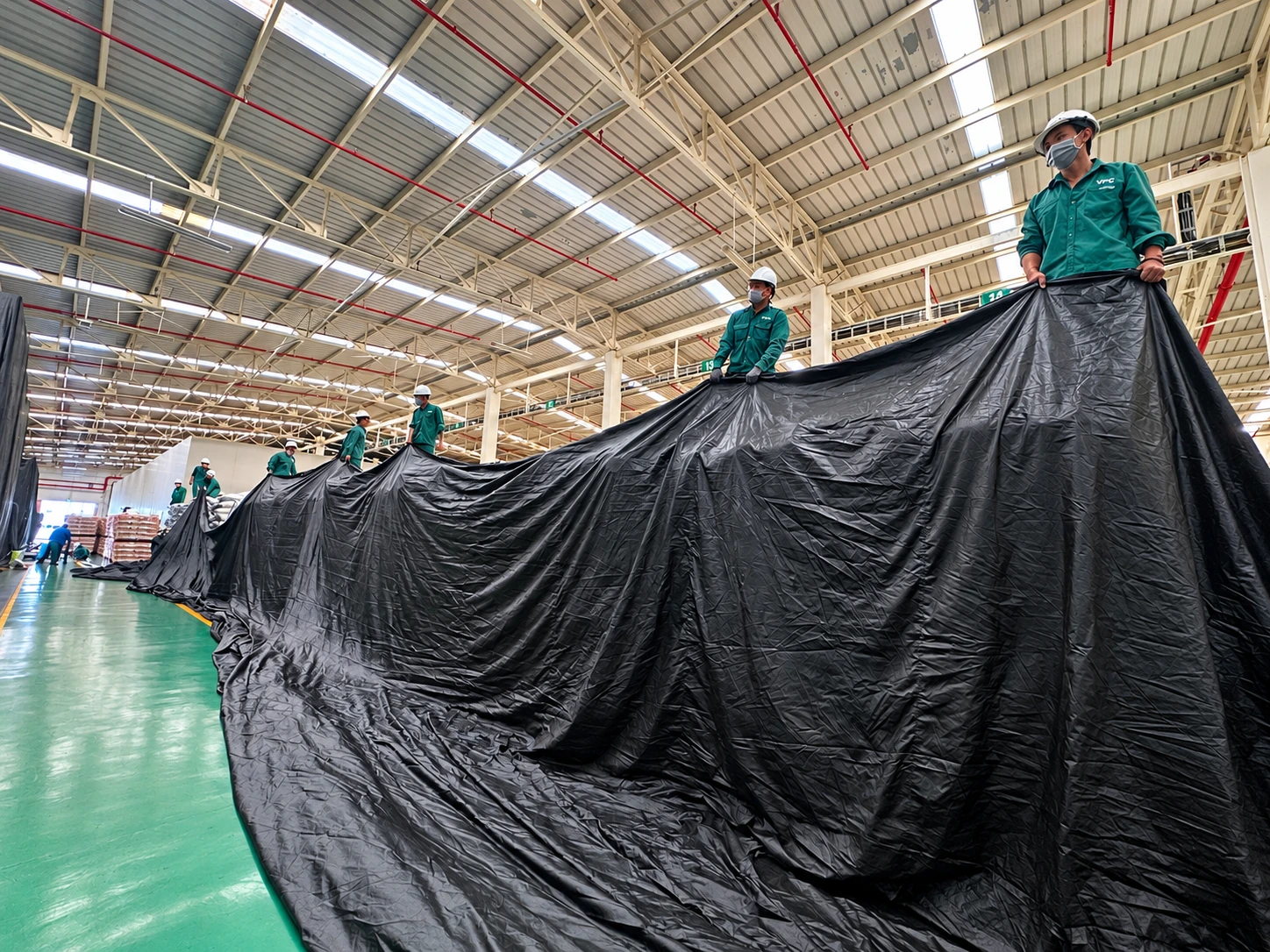 Workers arranging a fumigation tarpaulin in a warehouse